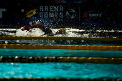 Schwimmer krault mit viel Gischt durch das Becken der Arena Games in München, dahinter der Arena-Games-Schriftzug