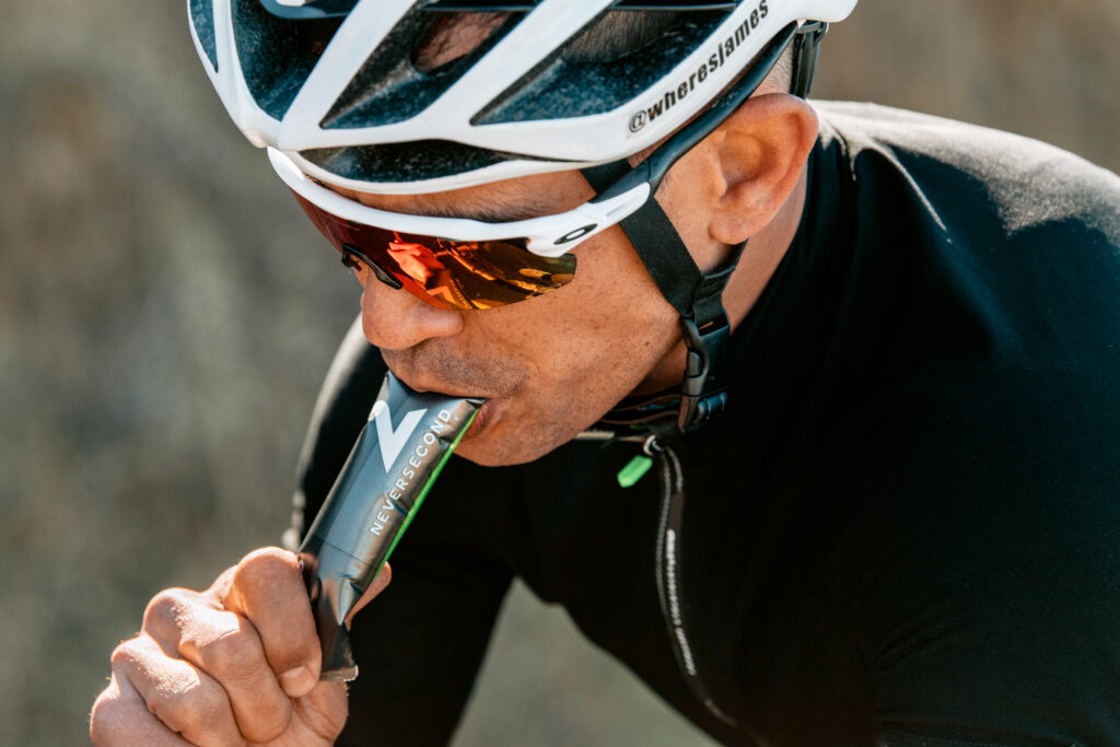 Radfahrer mit Helm und verspiegelter Sportbrille nimmt unterwegs ein Energiegel von Neversecond