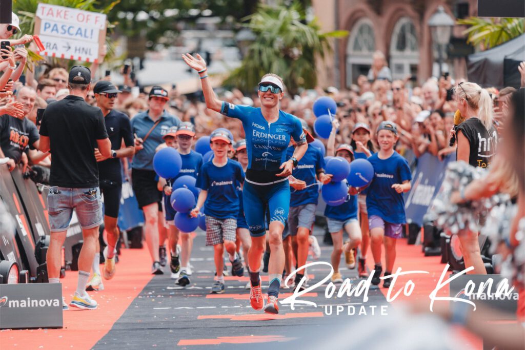 Daniela Bleymehl winkt im Zielkanal des Ironman Frankfurt, Kinder mit blauen Ballons laufen mit, Schriftzug Road to Kona