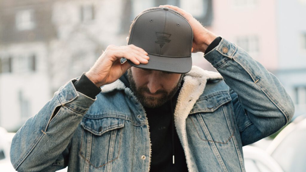 Mann in Jeansjacke mit Teddyfutter setzt die graue Pushing Limits Club Cap auf