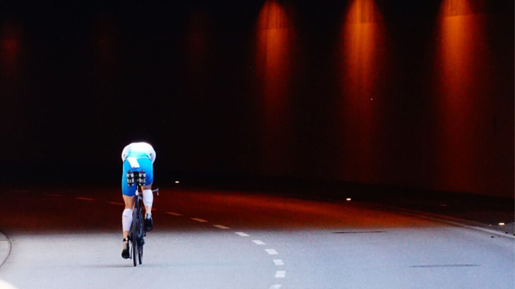 Triathlet auf dem Zeitfahrrad fährt beim Ironman Hamburg durch einen dunklen, rot beleuchteten Tunnel