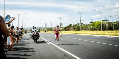 Läuferin mit Motorradbegleitung auf dem Highway bei der Ironman-WM auf Hawaii, links jubelnde Zuschauer