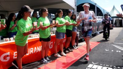Läuferin passiert bei der Ironman-WM 2023 auf Hawaii eine Verpflegungsstation mit Helferinnen in grünen Shirts