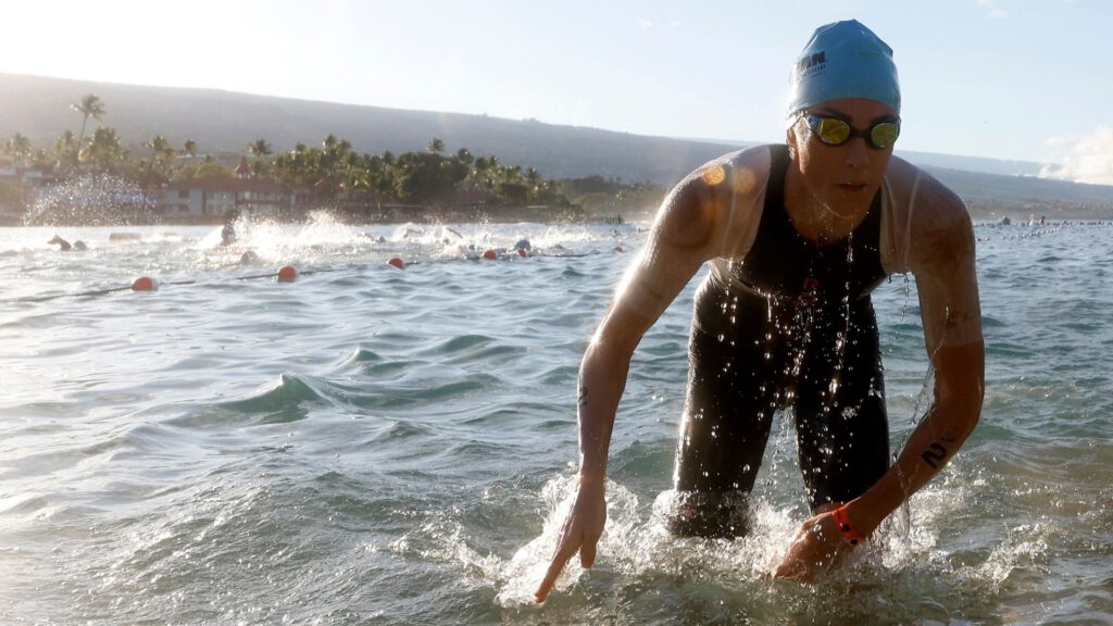 Triathletin mit hellblauer Badekappe watet bei der Ironman-WM 2023 in Kailua-Kona aus dem Meer