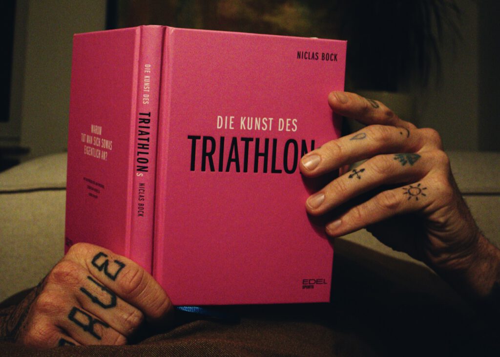 Hand hält das pinke Triathlon-Buch Die Kunst des Triathlons von Niclas Bock