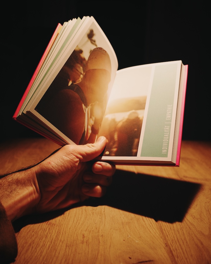 Aufgeschlagenes Buch Die Kunst des Triathlons mit ganzseitigem Foto, von einer Hand im warmen Licht gehalten